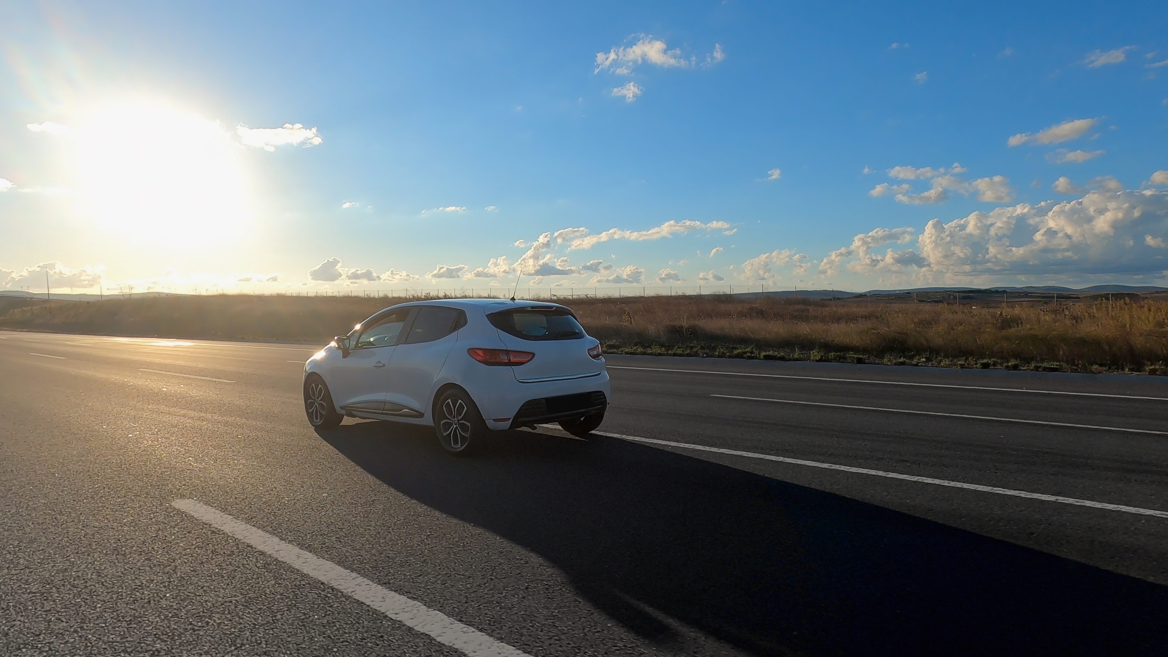 A white car driving down the road near some grass.