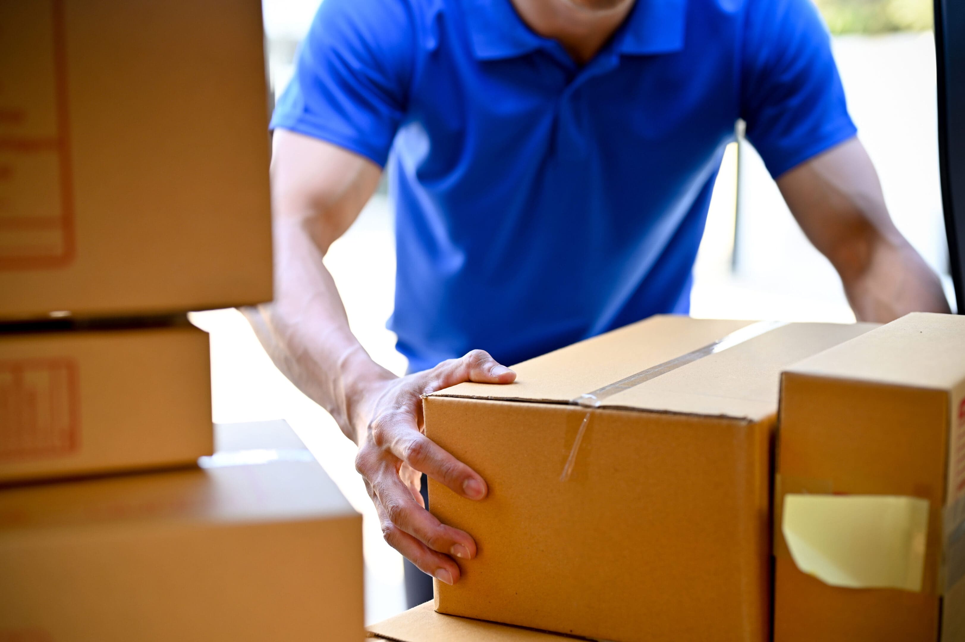 A man in blue shirt holding box while standing next to boxes.